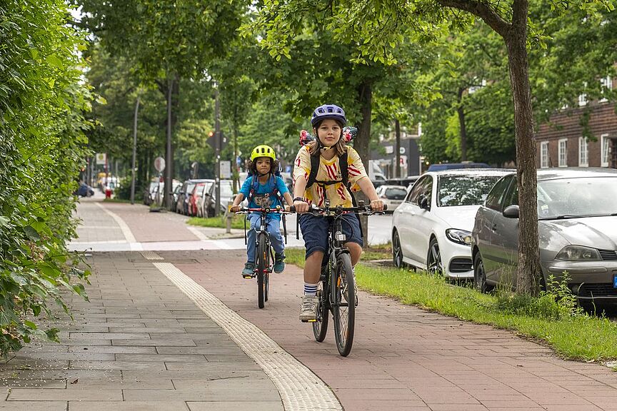 Kinder auf dem Schulweg Ein Mädchen fährt vor einem Jungen auf dem Fahrrad auf einem Radweg.
